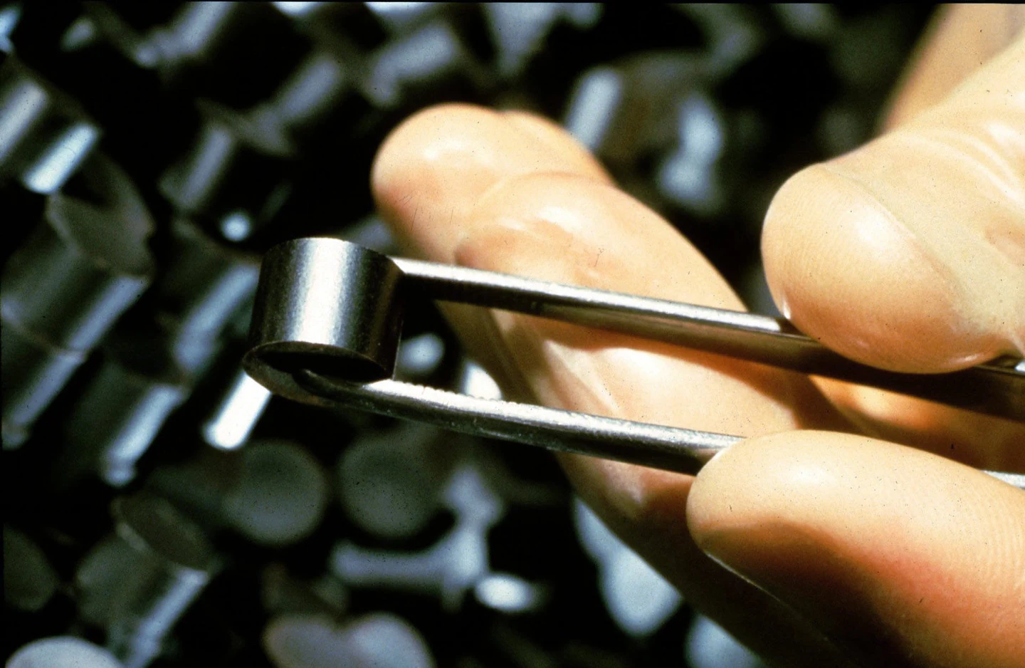 Uma pastilha real de combustível segura por uma pinça, junto aos dedos de quem a manuseia.
