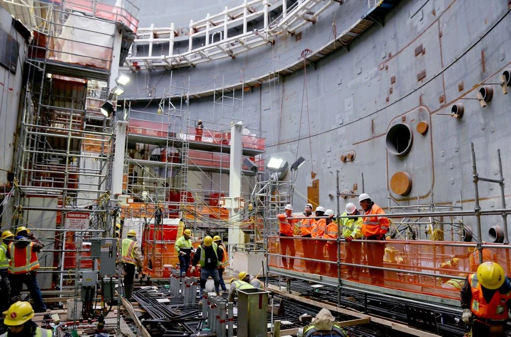Técnicos da NRC visitam o interior da contenção do reator 3 de Vogtle durante a construção. Veem-se pessoas, equipamentos e andaimes no interior da grande estrutura de aço.
