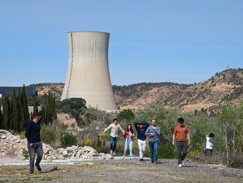Membros do Nuclear Vision Portugal caminham junto a uma torre de refrigeração durante uma visita a uma central nuclear